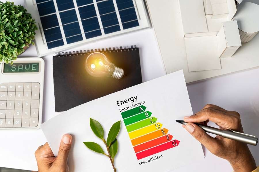 Une personne tient un document montrant une étiquette énergie avec des lettres colorées et une petite plante verte.